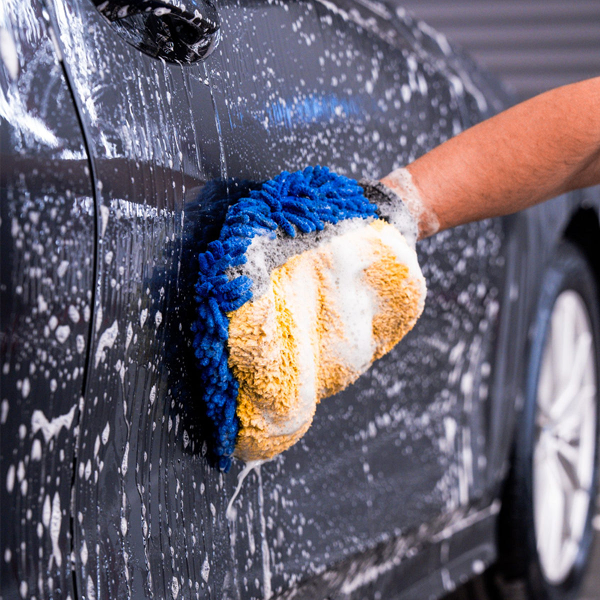 Person washing a car with a blue and yellow sponge