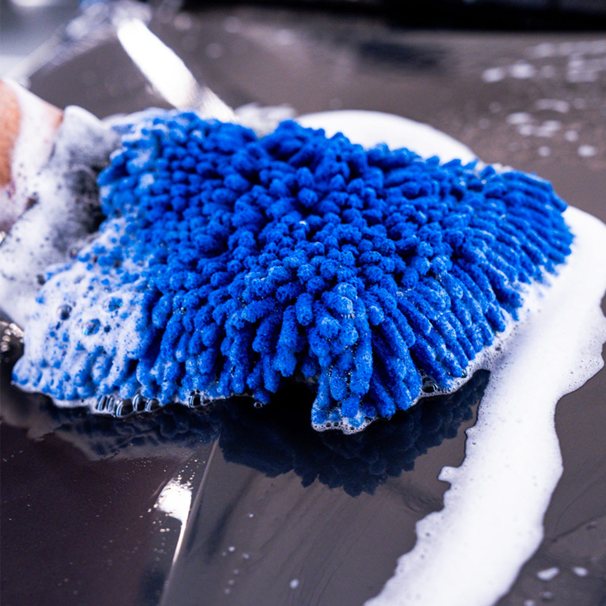 Blue microfiber mitt with soap suds on a car surface