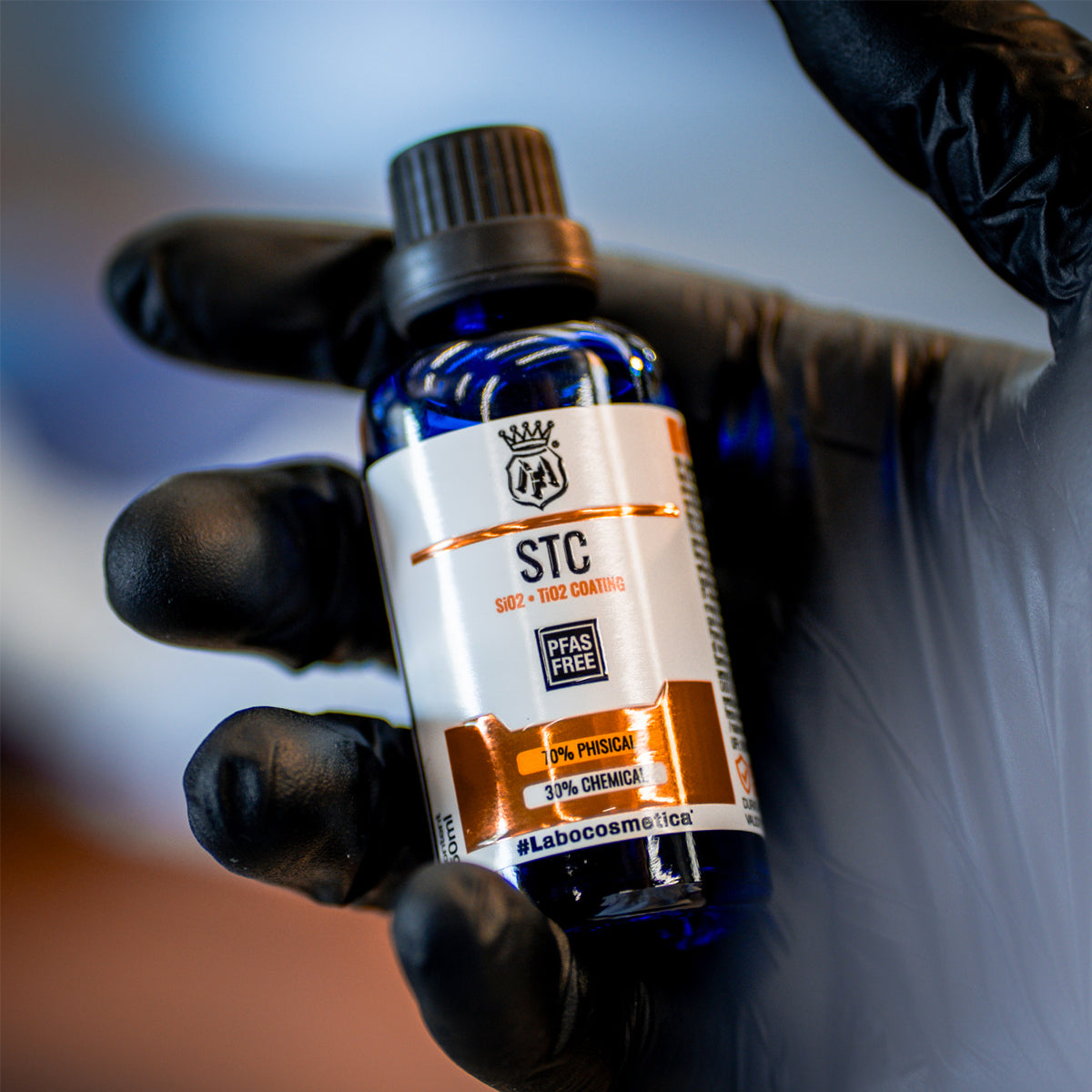 Bottle of STC product held by a gloved hand against a blurred background