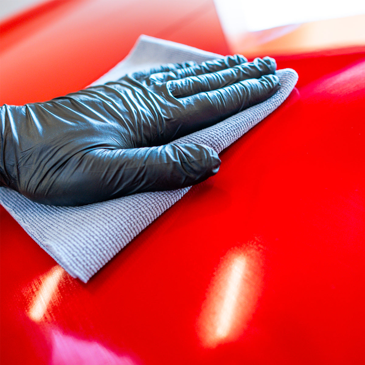 Hand wearing a blue glove cleaning a red surface with a cloth