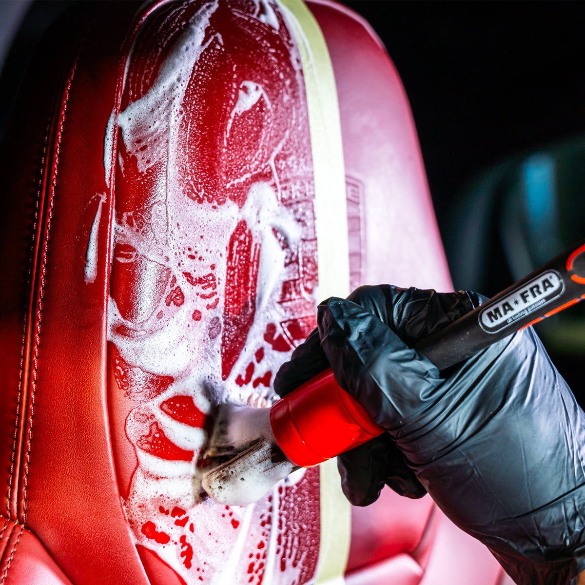 Person cleaning a red leather seat with a MA-FRA brush.