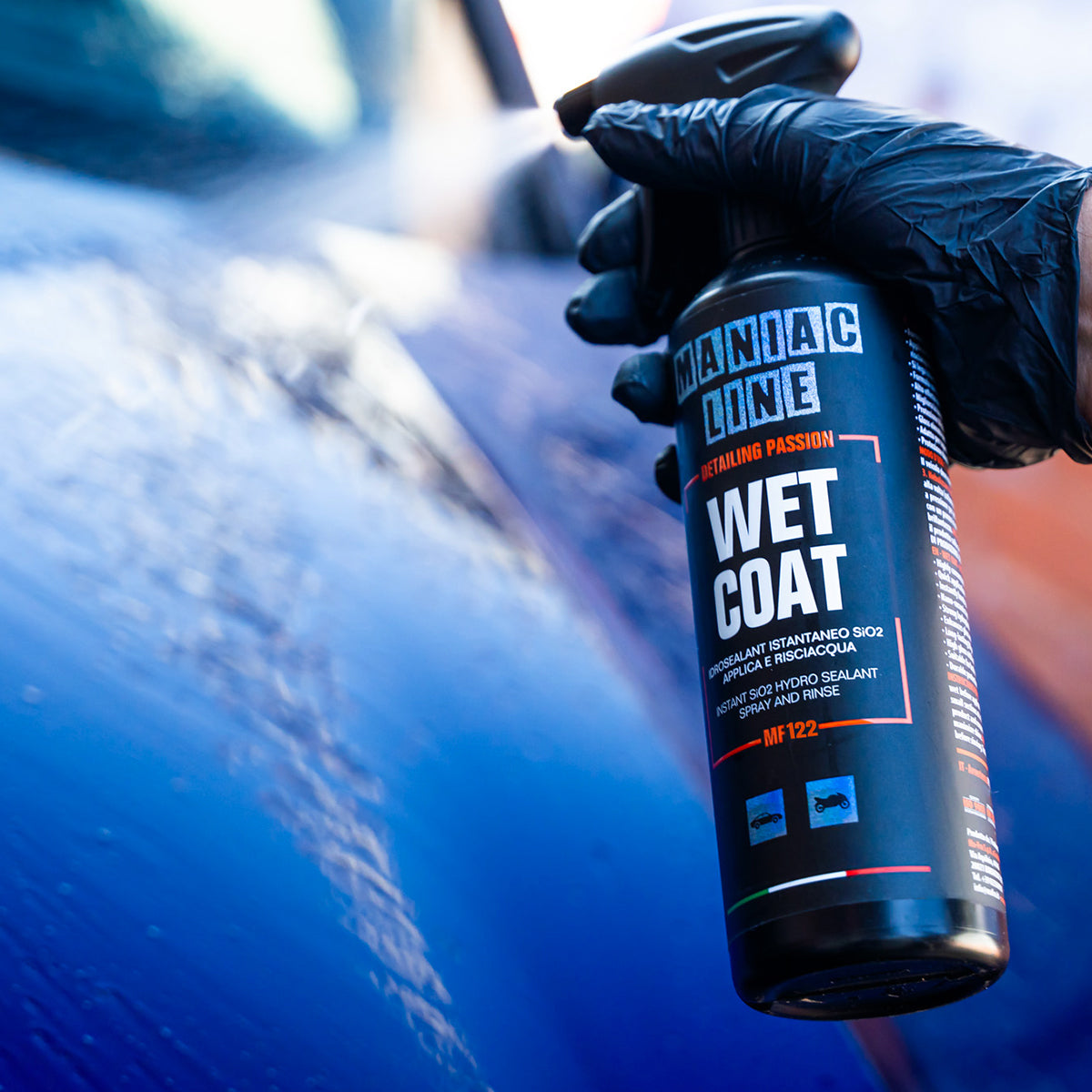 Hand holding a 'Maniac Line Wet Coat' can near a car